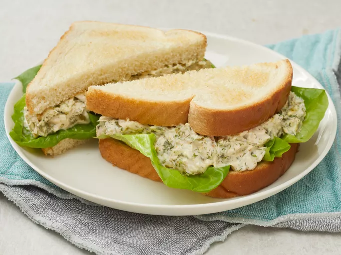 Low angle looking at two halves of Barbie's tuna salad sandwiches on a white plate