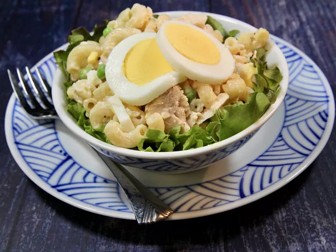 Maccaroni-tuna salad with sliced egg on top in blue patterned bowl above a similar plate
