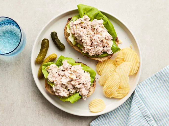 Looking down at a white plate of tuna salad with a side of chips and pickles.